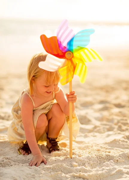 Menina bebê brincando com brinquedo colorido moinho de vento na praia — Fotografia de Stock