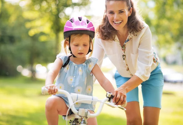 Happy mother helping baby girl riding on bicycle — Stock Photo, Image