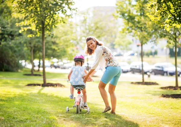 Feliz madre ayudando a bebé niña montar en bicicleta —  Fotos de Stock