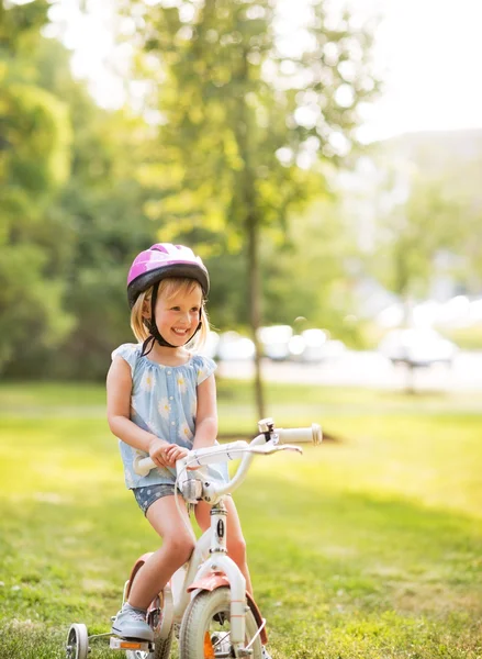 Portret van glimlachende babymeisje met fiets in park — Stockfoto