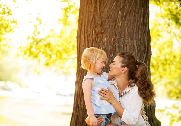 Retrato de madre feliz y niña de pie cerca del árbol — Foto de Stock