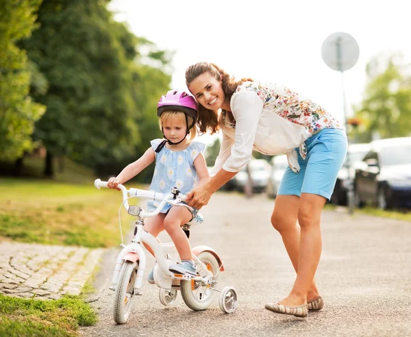 Мама помогает девочке кататься на велосипеде — стоковое фото