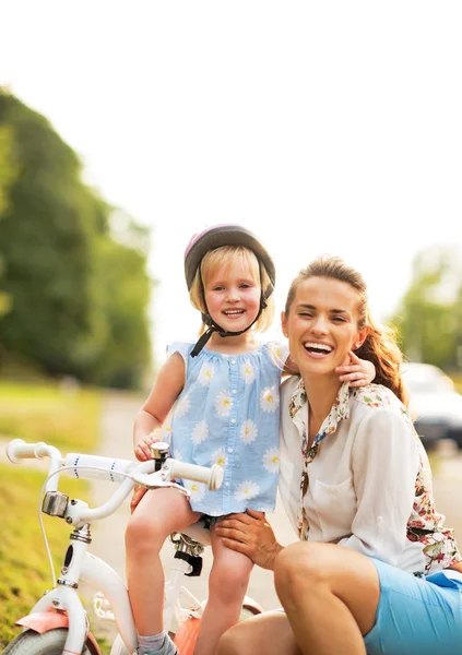 Portret van lachende moeder en babymeisje zit op fiets — Stockfoto