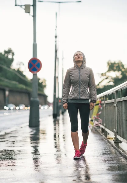 Портрет фитнеса молодой женщины, идущей по дождливому городу — стоковое фото