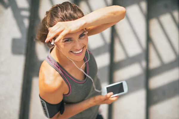 Портрет улыбающейся фитнес-девушки с сотовым телефоном на улице — стоковое фото