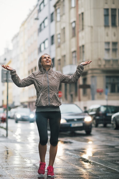 Full length portrait of happy fitness young woman catching rain 