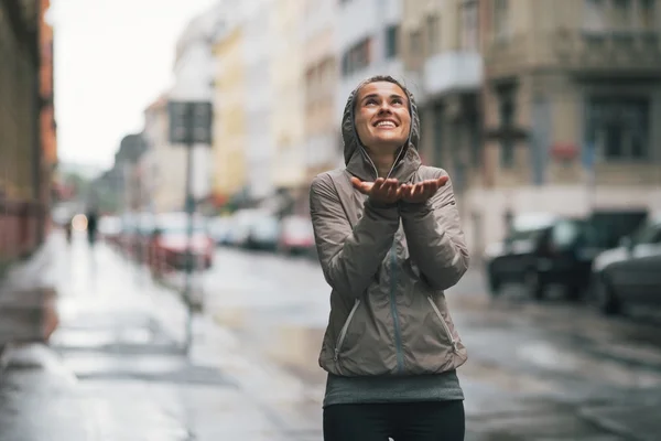 Jovem fitness feliz pegando gotas de chuva na cidade — Fotografia de Stock