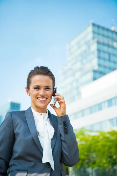Smiling business woman talking mobile phone in front of office b — Stockfoto