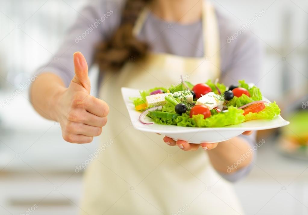 Closeup on young housewife showing greek salad and thumbs up
