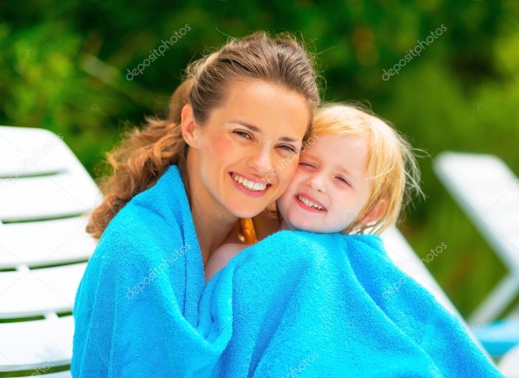 Portrait of smiling mother and baby girl wrapped in towel sittin