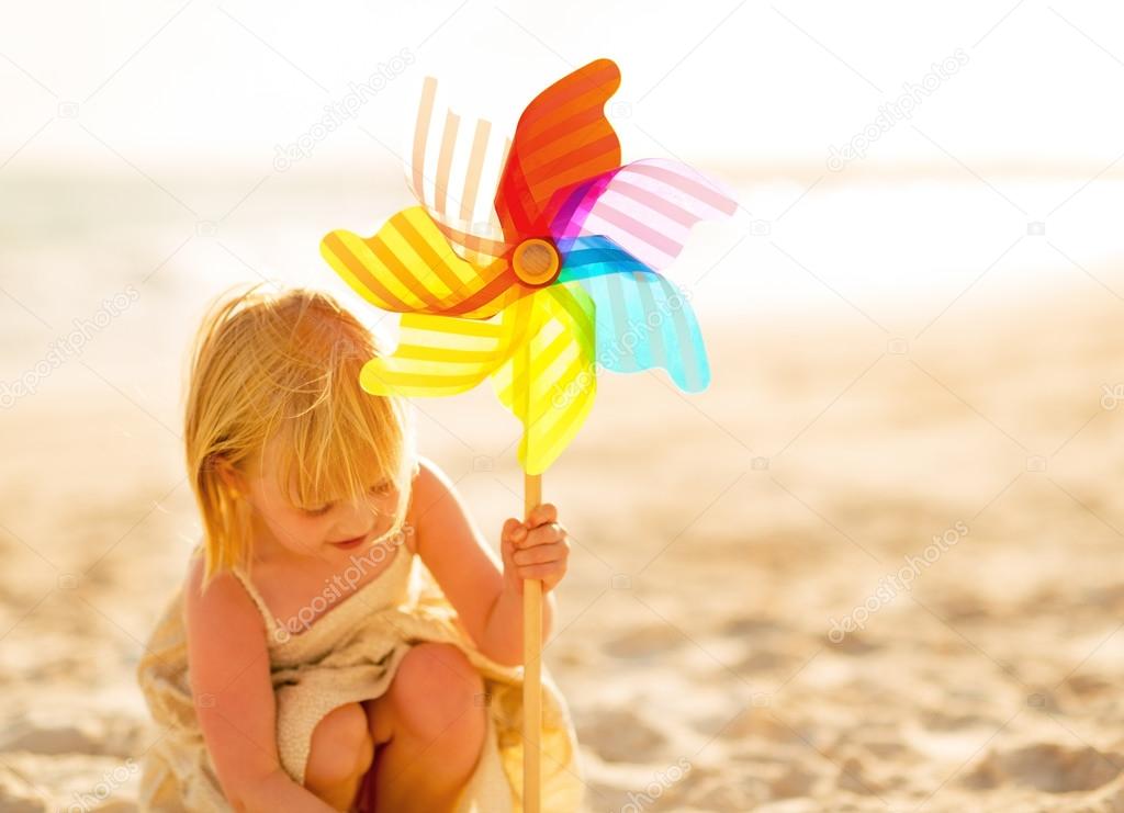 Baby girl playing with colorful windmill toy on beach