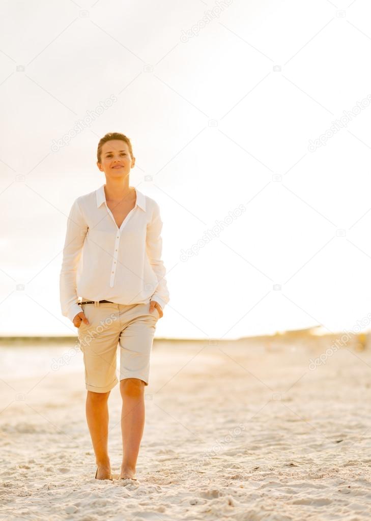 Portrait of happy young woman walking on beach at the evening