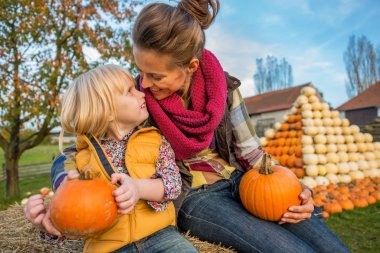 Smiling mother and child sitting on haystack with pumpkins clipart