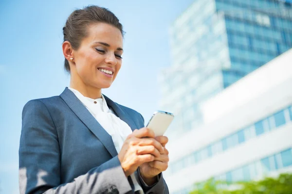 Happy business woman writing sms in front of office building — Stockfoto