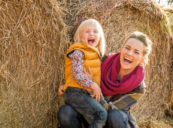 Portræt af smilende mor og barn nær høstak - Stock-foto