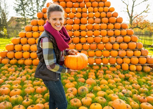 Portrait of smiling young woman holding pumpkin in front of pump — Stock Photo, Image