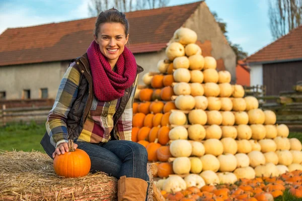 Portret van een jonge vrouw zittend op hooiberg met pompoen voor pompoen piramide — Stockfoto