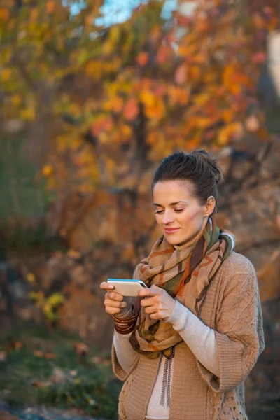 Glückliche junge Frau im Herbst abends draußen SMS schreiben — Stockfoto