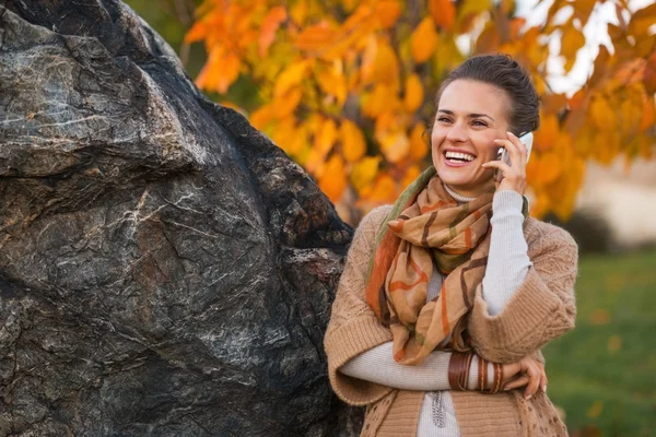 Улыбающаяся молодая женщина разговаривает по телефону осенью на открытом воздухе накануне — стоковое фото
