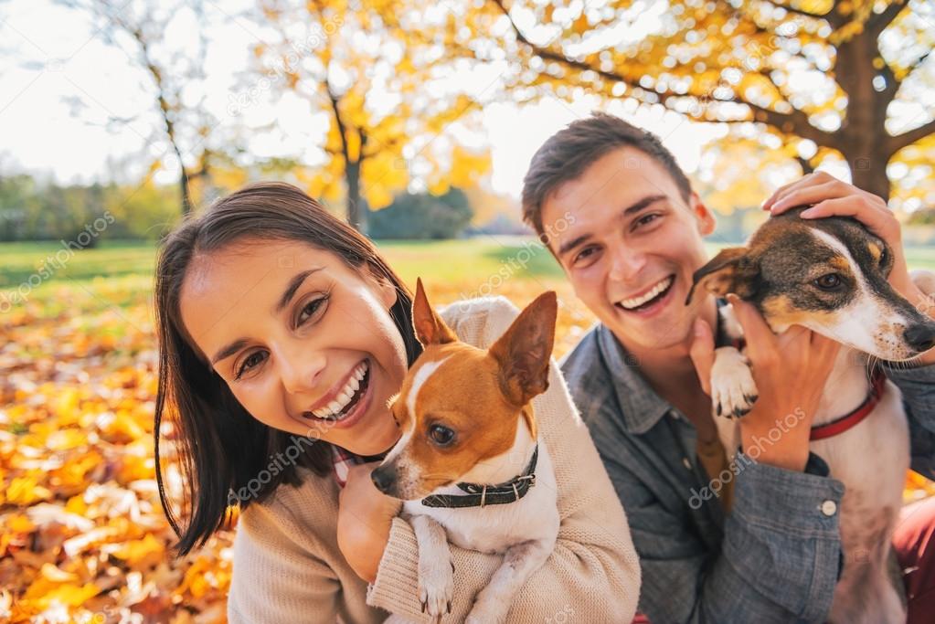 Portrait of smiling young couple with dogs outdoors in autumn pa