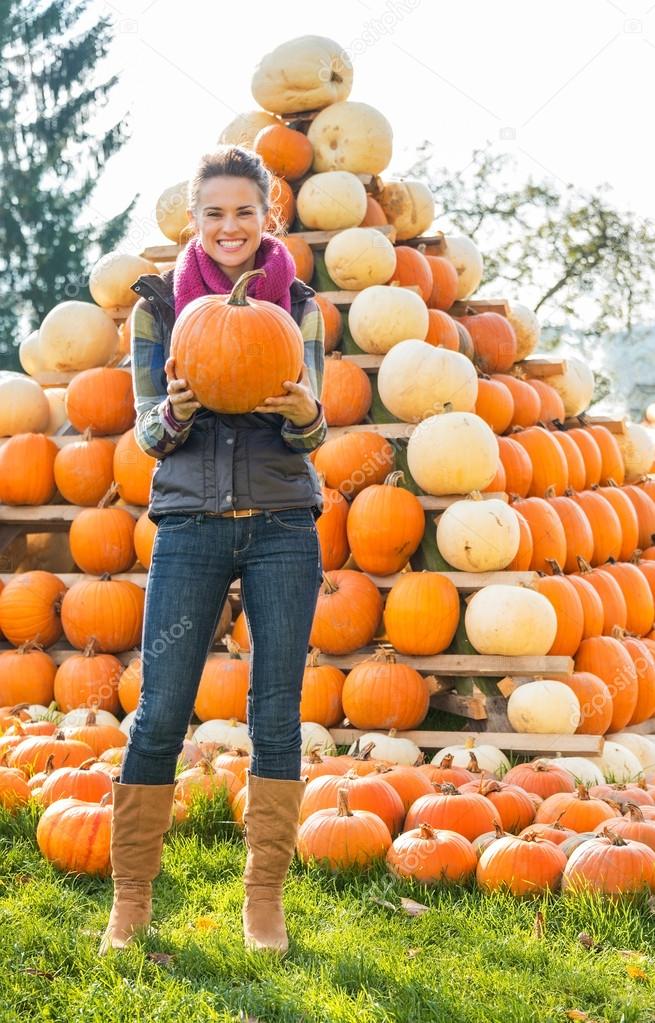Portrait of happy young woman holding pumpkin in front of pumpki