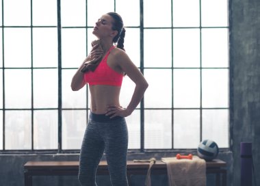 Fit woman in profile wiping sweat off neck in loft gym