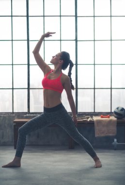 Fit barefoot woman in profile doing yoga stretch in loft gym