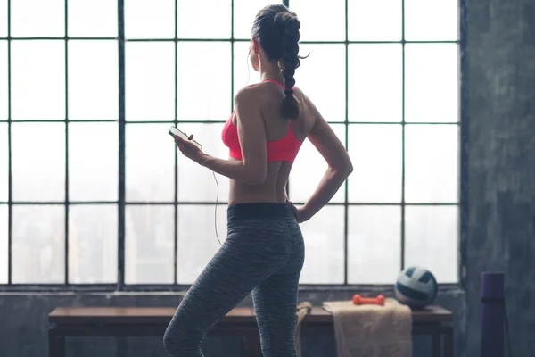 Fit woman standing in gym looking out window listening to music — Stockfoto