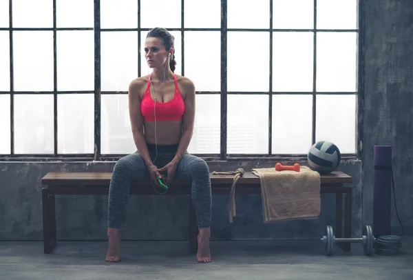 Fit woman sitting on bench in workout gear listening to music — 스톡 사진