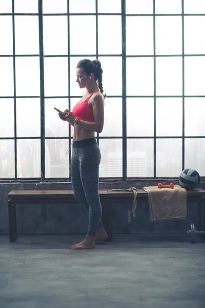 Fit woman selecting music on device in loft gym — Stockfoto