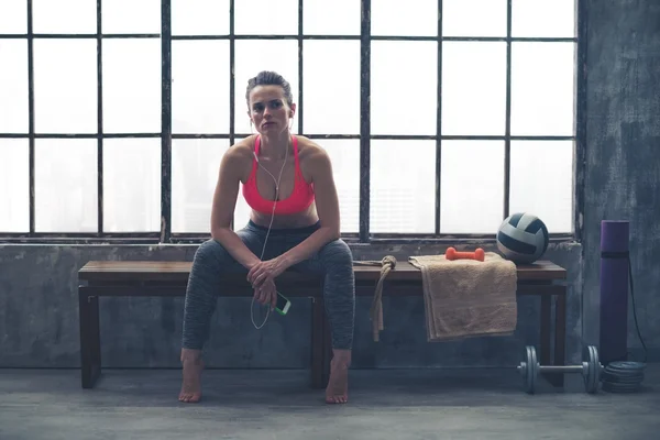 Woman sitting on bench by window in loft gym listening to music — Φωτογραφία Αρχείου