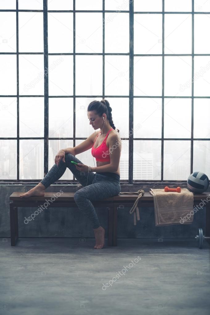 Woman in workout gear choosing workout music in loft gym