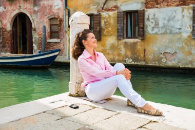 Happy woman sitting and relaxing on pier in Venice