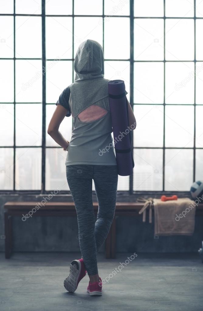 Woman standing relaxing in gym seen from behind wearing hoodie