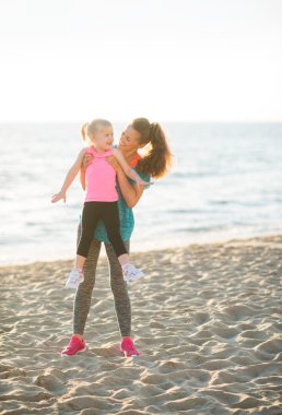 Fit young mother lifting young daughter up on beach at sunset