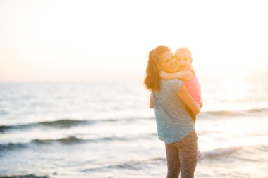 Mother and daughter in workout gear hugging at sunset on beach