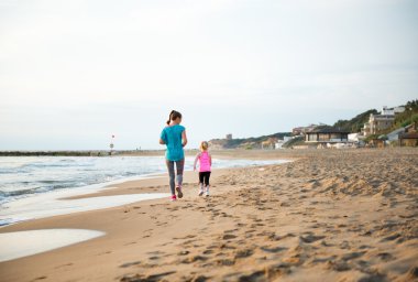 Seen from behind, mother and daughter running on the beach
