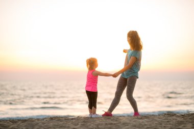 Fit young mother and daughter on the beach, looking out to sea