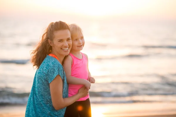 Portræt af glad ung mor og datter på stranden ved solnedgang - Stock-foto