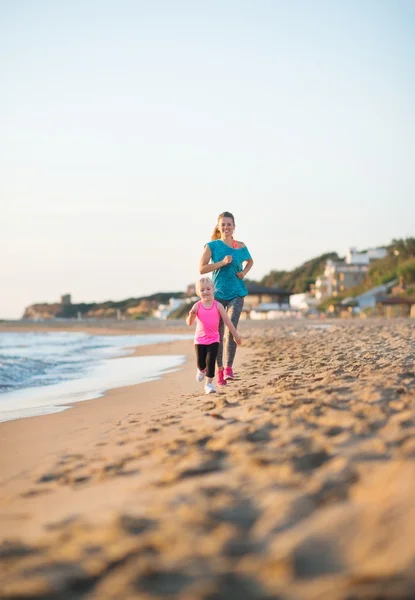 Young mother running behind daughter on the beach at sunset — Stock Photo, Image