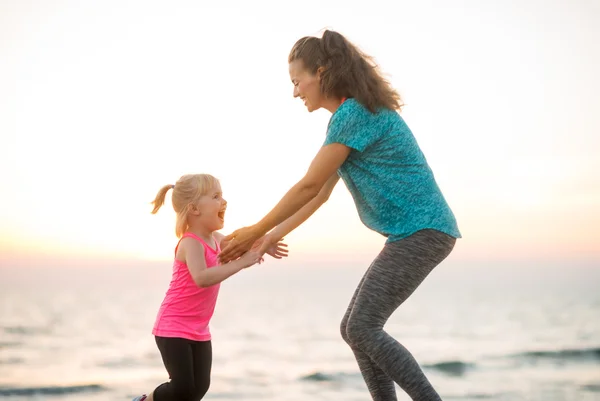 Fit young mother and daughter playing on the beach at sunset — Stock fotografie