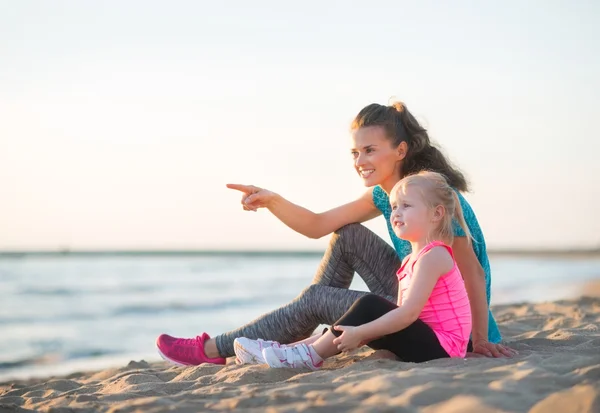 Pointing mother with daughter in workout gear sitting on beach — 图库照片