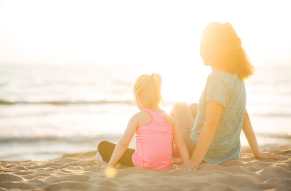 Mother smiling over shoulder sitting next to daughter on beach — Stockfoto