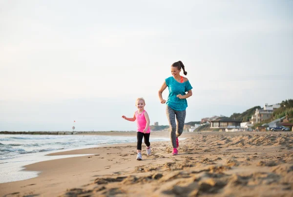 Mother and daughter running on the beach at sunset — Stockfoto