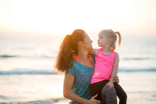 Young passen moeder lacht met dochter op haar knie op strand — Stockfoto