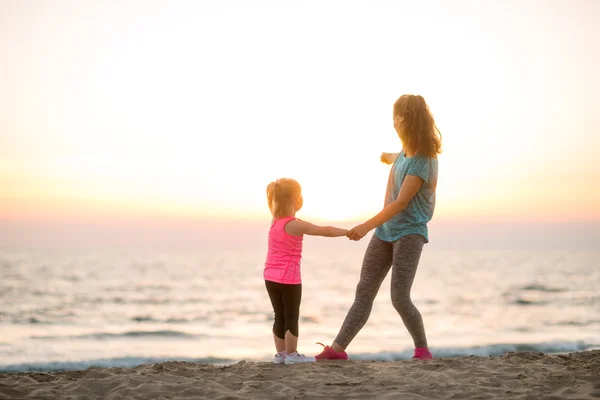 Fit young mother and daughter on the beach, looking out to sea — Stock fotografie