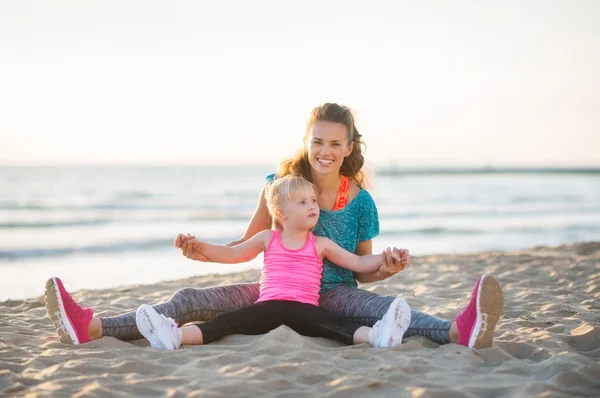 Sonrientes madre e hija sentadas juntas estirando los brazos — Foto de Stock