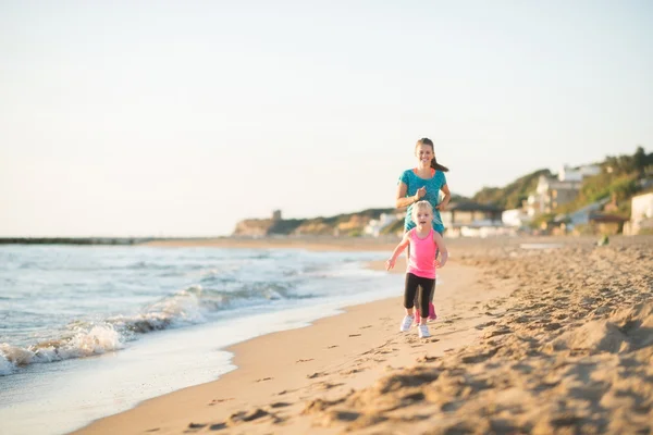 Mother and daughter running along water on beach at sunset — 图库照片