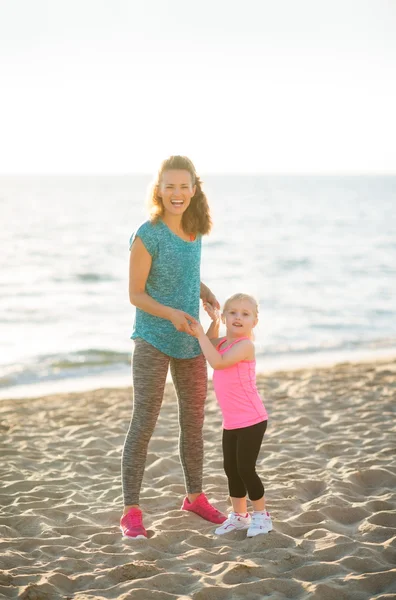 Glückliche junge Mutter und Tochter am Strand Händchen haltend — Stockfoto