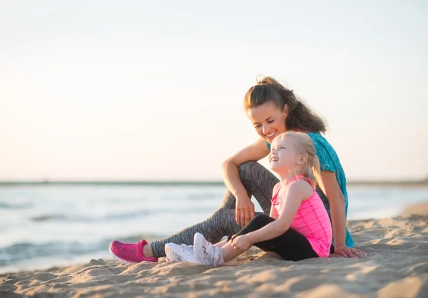 Lykkelig ung mor og datter taler og sidder på stranden - Stock-foto